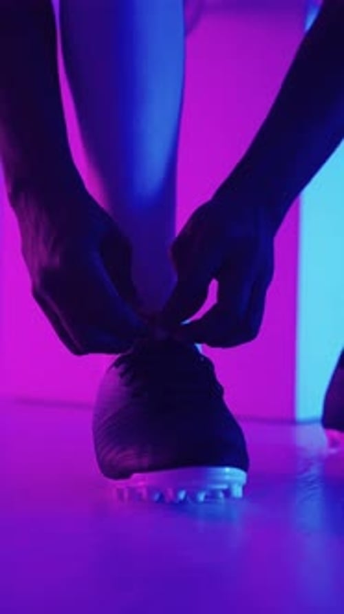 Vue rapprochée d'un joueur de football se préparant pour un match en nouant des lacets sur des crampons dans un violet vif