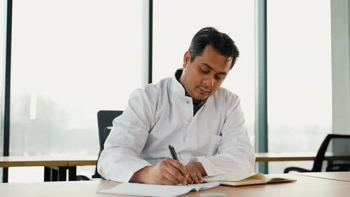 Stressed Frustrated Indian Doctor with Headache Sitting Alone at Work Desk in Hospital Sad Young Gp
