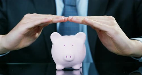 A man dressed in a suit and tie, puts money into the piggy bank. Concept: Pension, savings, invest