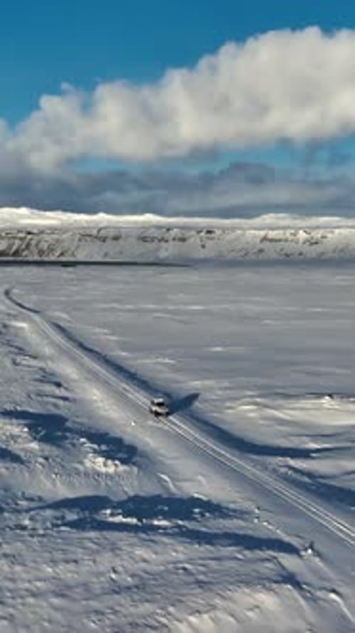 Vertical aerial view of a lone vehicle driving along the frozen shore of Kleifarvatn on Iceland’s