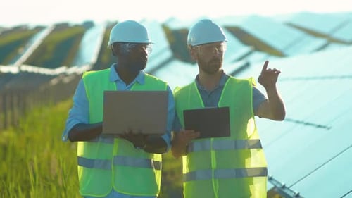 Close Up at Sunlight Men Use Laptop on the Solar Farm in Special Uniform Walking Discuss the