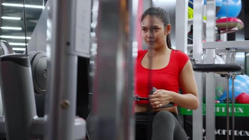 Young asian woman workout with strength training and determination with fitness gym machines.