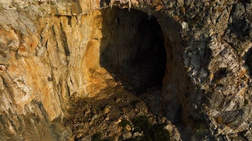 Drohne rotiert um eine in eine Bergwand gehauene Grotte, goldene Stunde in Griechenland