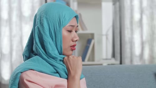 Feche uma mulher muçulmana encostada em um sofá pensando em algo enquanto trabalha em um laptop em casa