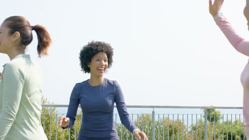 Diverse female workout partners on rooftop upon meeting high-fiving then sharing tips near railing