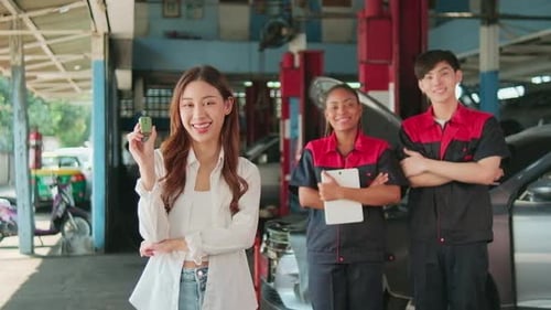 Young female customer shows car key with automotive mechanic workers at garage.