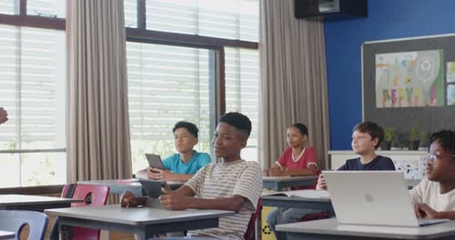 In school classroom, students using tablets and laptops, engaging with teacher