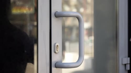 Closeup of a Hand in a Purple Sleeve Pushing a Lightcolored Door Handle Focusing on the Grip and