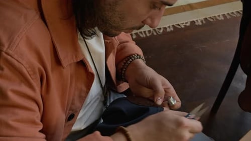 Crafty Young Man Sewing Elbow Patch onto Preowned Jacket on Workshop
