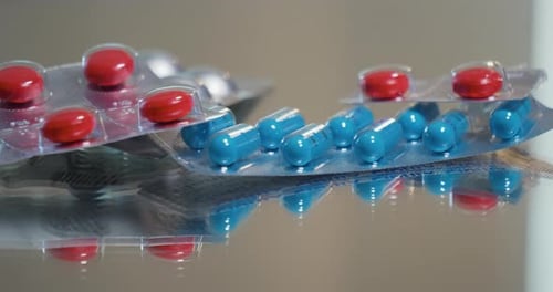 Panning view of blue, red and white pills and prescription drugs on a reflective table.