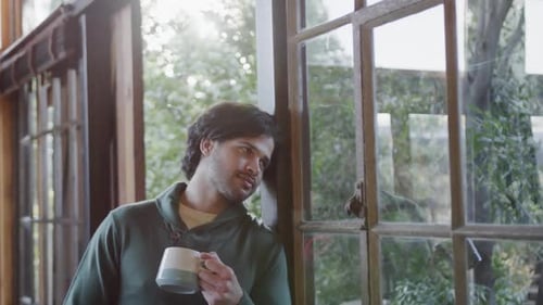 Caucasian man holding cup of coffee and looking out window at home, slow motion, slow motion