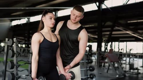 Woman Lifts Weights With Trainer in Gym