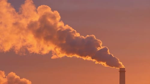 A Solitary Factory Smokestack Emits Swirling Smoke As the Sun Sets Bathing the Scene in Gold
