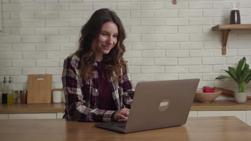 Smiling Woman Typing on Laptop at Kitchen Table