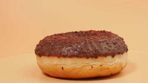 Rotating Chocolate donut with chocolate chips on an orange background.