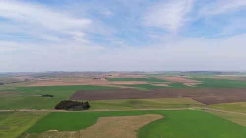 Aerial View of Agricultural Fields with Green and Brown Patches in Countryside, cloudy blue sky