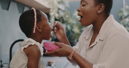 Woman Feeds Child with Bowl and Spoon Indoors