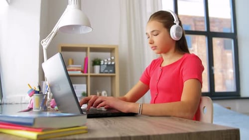 Teenage girl with headphones using laptop at desk