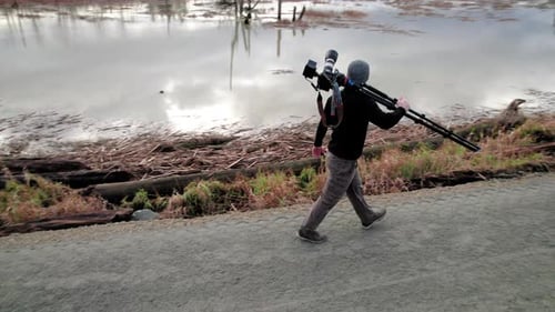 Photographer Walks Beside Marsh with Camera Equipment