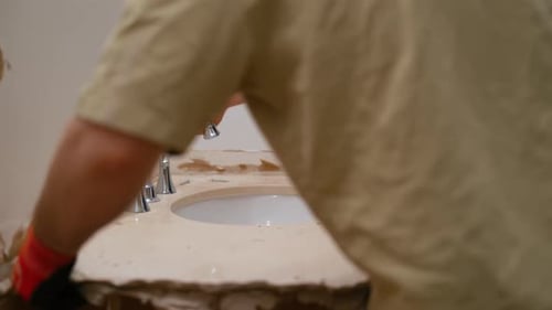 Construction Worker Removing an Old Bathroom Sink During Renovation Demolition Phase of Interior
