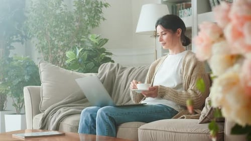 Woman Works on Laptop and Drinks Coffee at Home