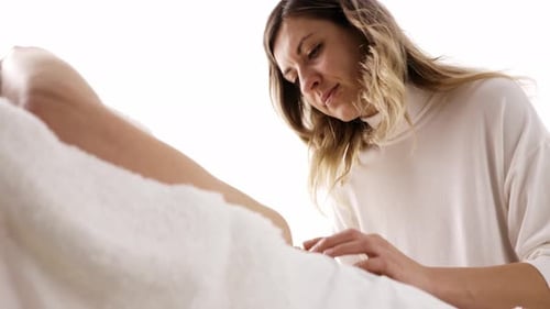 Side View of Young Masseuse Massaging Face of Young Woman Lying on Sofa
