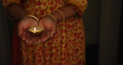 Holding lit diya, Indian woman in traditional dress celebrating festival at night