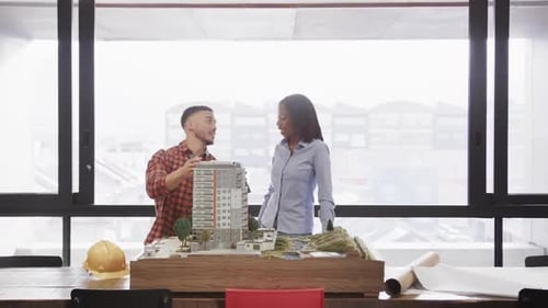 Diverse male and female architect discussing architectural model in office, slow motion
