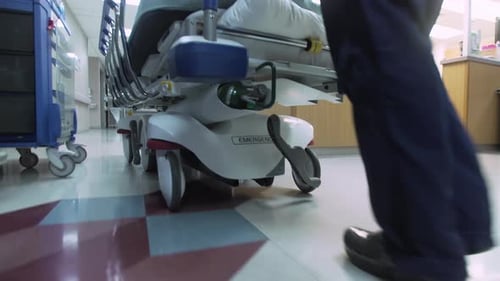 Emergency Room Nurse pushes stretcher / gurney down Hospital Emergency Room hallway. Camera follows