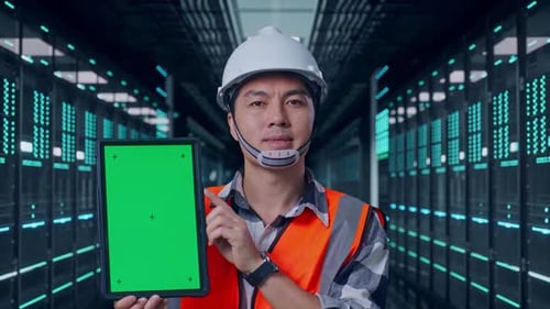 Nahaufnahme eines asiatischen männlichen Ingenieurs, der lächelt und ein Greenscreen-Tablet im Rechenzentrum zeigt