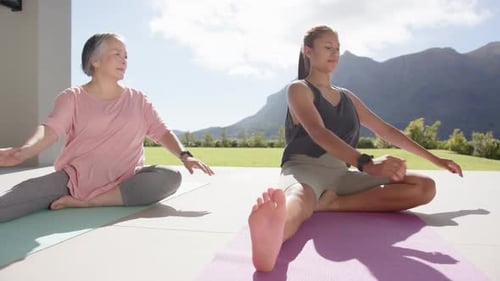 Practicing yoga, women stretching on mats outdoors with mountain view