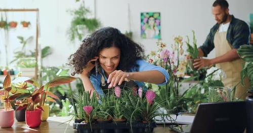 African american female worker of flower shop sitting at table and calling on smartphone and caring