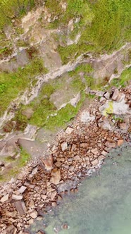 Coastline with high rocks and multiple boulders at the beach. Drone footage rising over the shore.