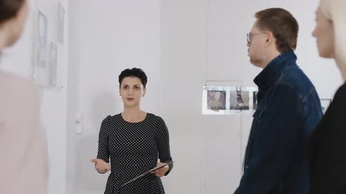 A Woman Gallery Owner Tells Visitors About the Paintings Presented at the Exhibition