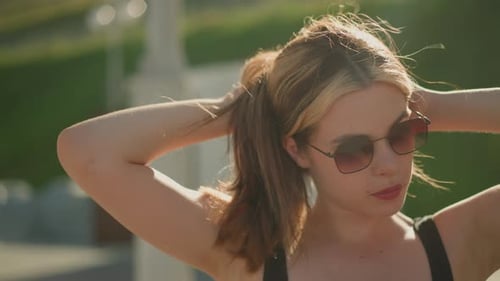 Young Woman Tying Hair Back in Sunlight