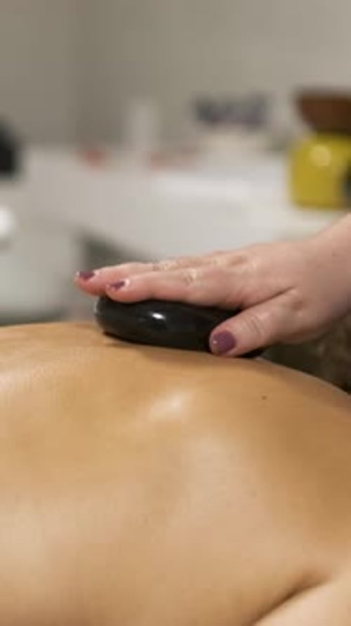 Masseuse Delivering a Relaxing Hot Stone Massage in a Tranquil Spa Setting Vertical