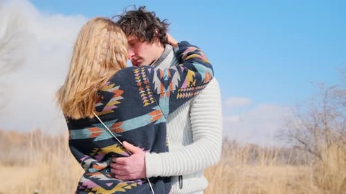 Couple lovingly embraces in autumn field, foreheads touching beneath blue sky.