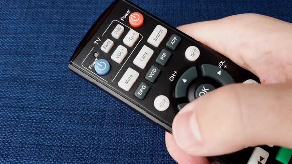 Pressing the TV channel up button on the tv remote control. Watching ...