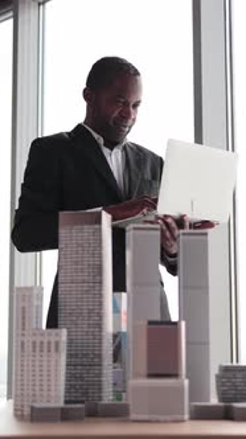 Man in Suit Working on Laptop with Building Models