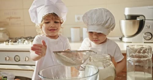Two Toddlers in Chef Hats Cooking Smiling and Sharing in the Kitchen