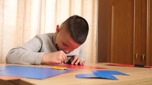 Boy Drawing with Marker on Red Paper at Table