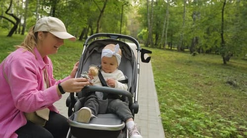 Mother in the Park with Her Little Daughter in a Baby Carriage Mom Playing with Her Child Outdoors