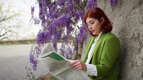 Woman Reading Newspaper by Flowers on Cloudy Day