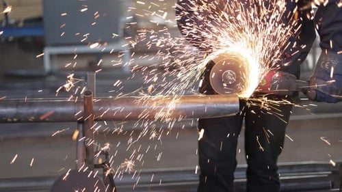 Hardworking Male in Protective Clothing Cutting Long Pipe with Angle Grinder