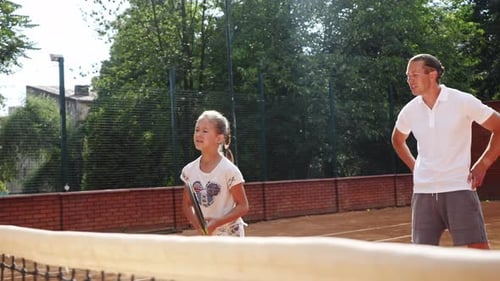Girl Receives Tennis Coaching from Man on Sunny Day