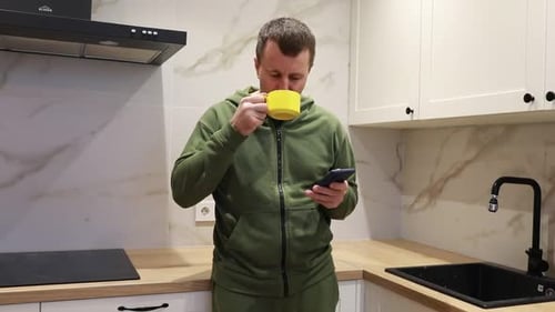 Man Drinks Coffee and Uses Phone in Kitchen