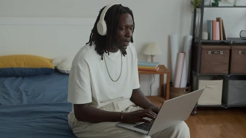 Man Using Laptop on Bed with Headphones