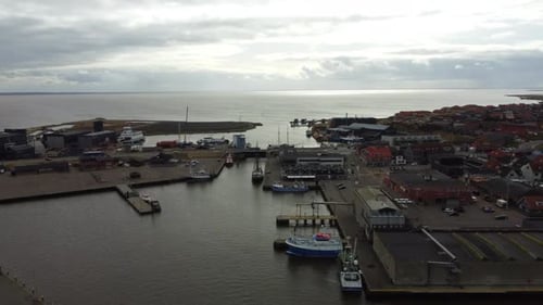 Cinematic Aerial View of Coastal Town Harbor with Boats and Modern Waterfront Buildings