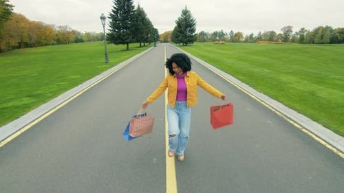 AfroAmerican Happy Woman with Paper Bags Jumping Spinning Around on a Road