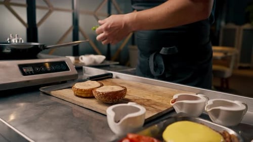 A close-up of a chef preparing a burger with beef patty with vegetables and cheese in the kitchen